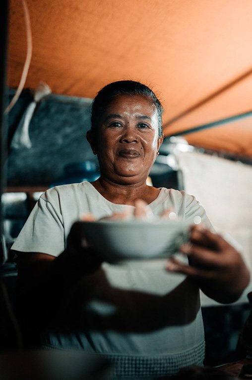 A picture of a local in Bali holding a bowl with a tasty Bali traditional food dish inside