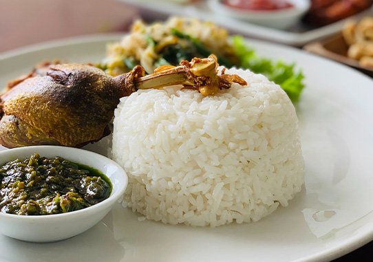 A picture of a meal in Bali with rice meat and vegetables.