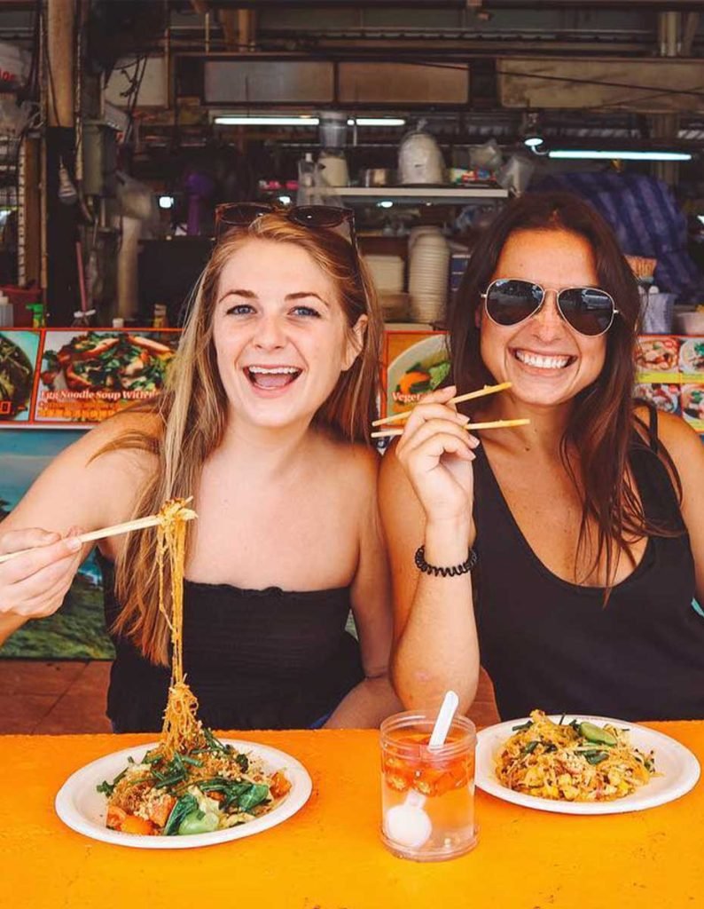 A picture of two girls eating street food in a night market.