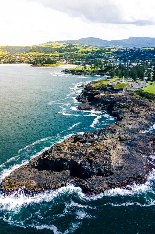 Aerial view of Kiama coastline with rugged cliffs and white lighthouse overlooking the Tasman Sea in New South Wales, Australia