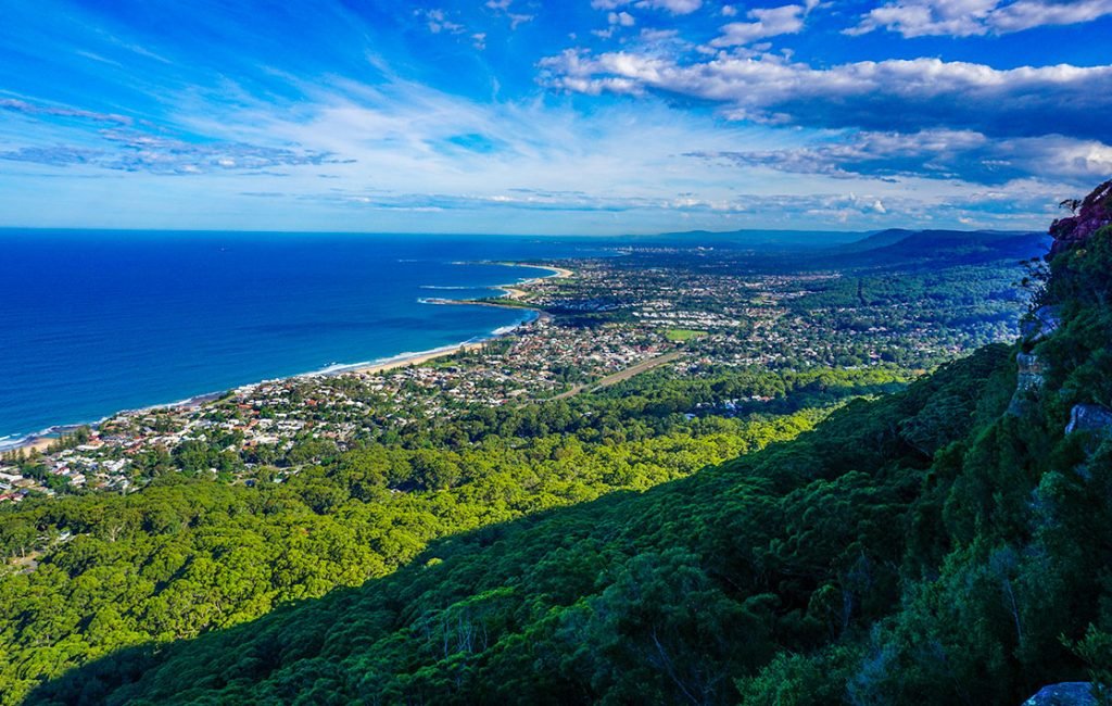 Aerial perspective of Wollongong's coastline with its expansive sandy beach, surf waves, and a cliff-side community in Australia.
