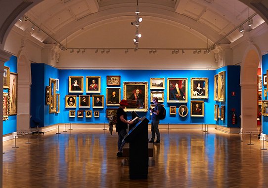 A picture of a room in the gallery with paintings on a blue wall. 