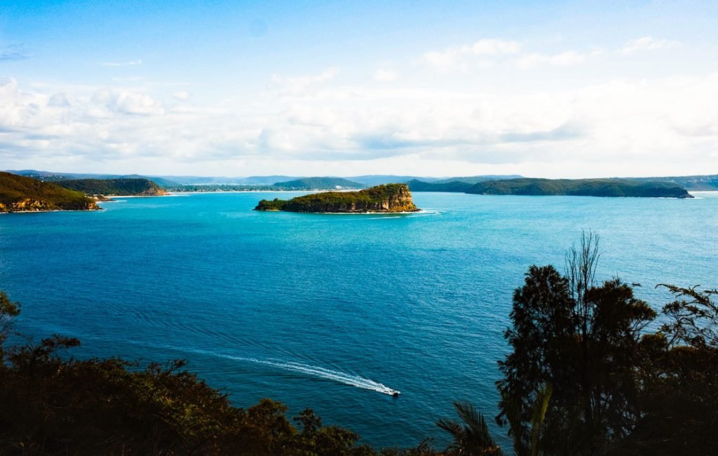 Scenic overlook of the calm blue waters of Ku-ring-gai Chase National Park with a speedboat in the distance and dense foliage framing the shores