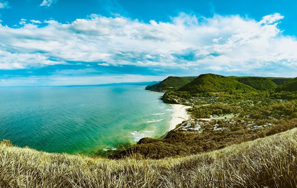 Panoramic view of the sunlit Royal National Park coastline with its pristine beaches and dense greenery, reflecting Australia's natural beauty