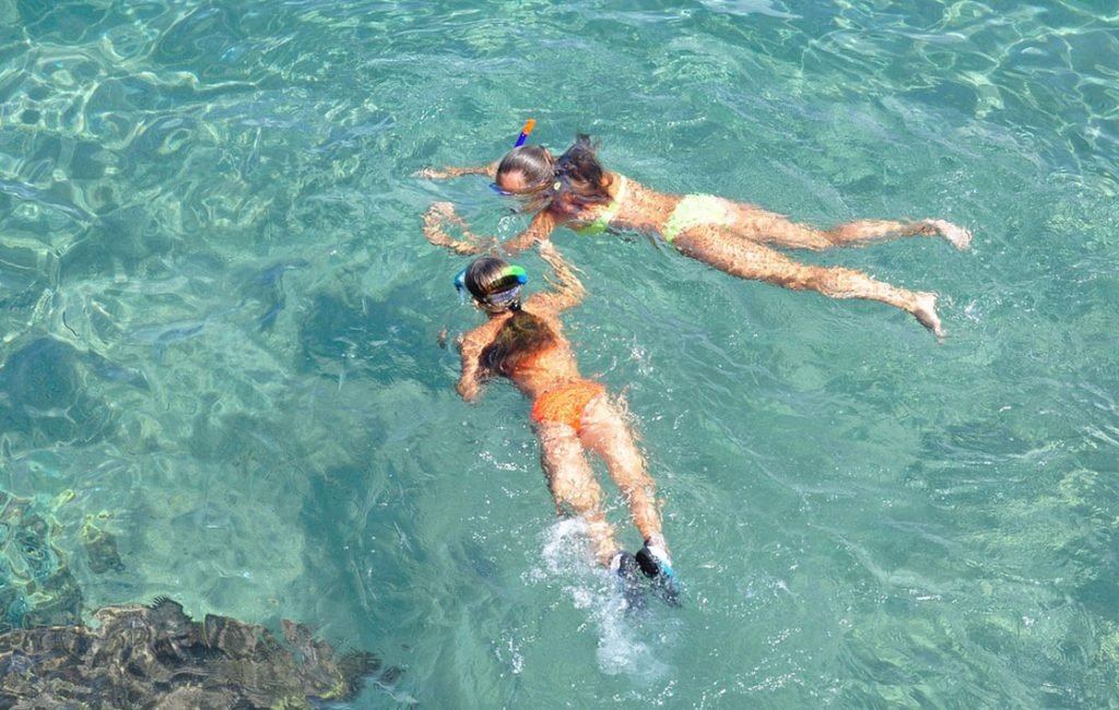 Two snorkelers exploring the clear turquoise waters over a coral reef, with a vibrant underwater world visible below them