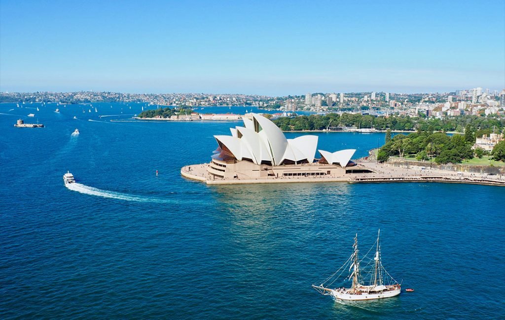 A picture of the view from Sydney Harbour Bridge. You get a view of the Opera House and the city in the background.