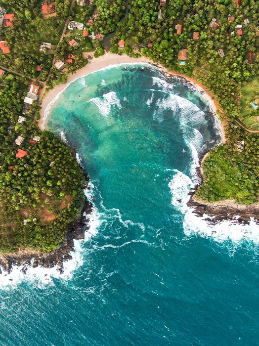 Aerial view of Hiriketiya Bay with its turquoise waters and lush tropical vegetation, showcasing a serene beachside community