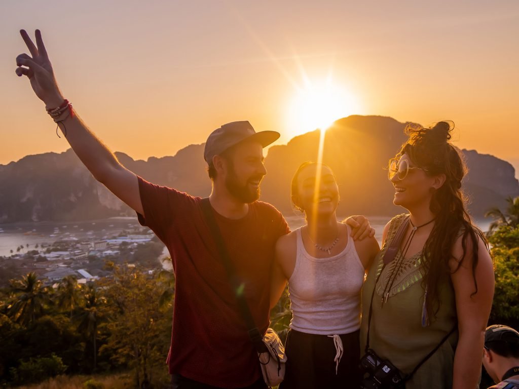 Three travellers enjoying a sunset at Phi Phi viewpoint, with one giving a peace sign, as they all smile and bask in the warm golden light with a scenic backdrop