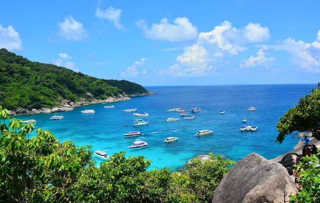 Scenic overlook of a vibrant blue sea dotted with boats near a tropical island with lush vegetation and rocky shoreline