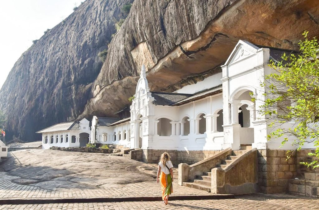 A woman walking towards a historical white temple at the base of a massive rock formation, representing cultural exploration