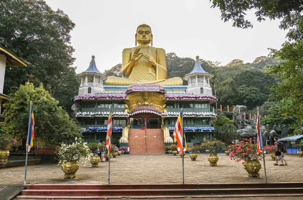 A golden Buddha statue towering over the entrance of a colorful temple, indicative of religious architecture and serenity