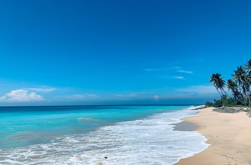 A pristine tropical beach with a clear blue sky, the ocean in varying shades of blue, and waves gently breaking on the sandy shore.