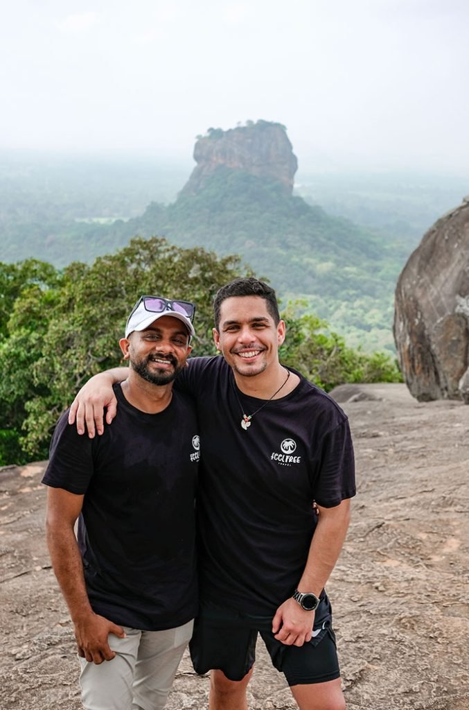 Two men smiling for the camera with a misty mountain peak in the background, symbolizing friendship and travel. The rock is one of the best things to do in Sigiriya.
