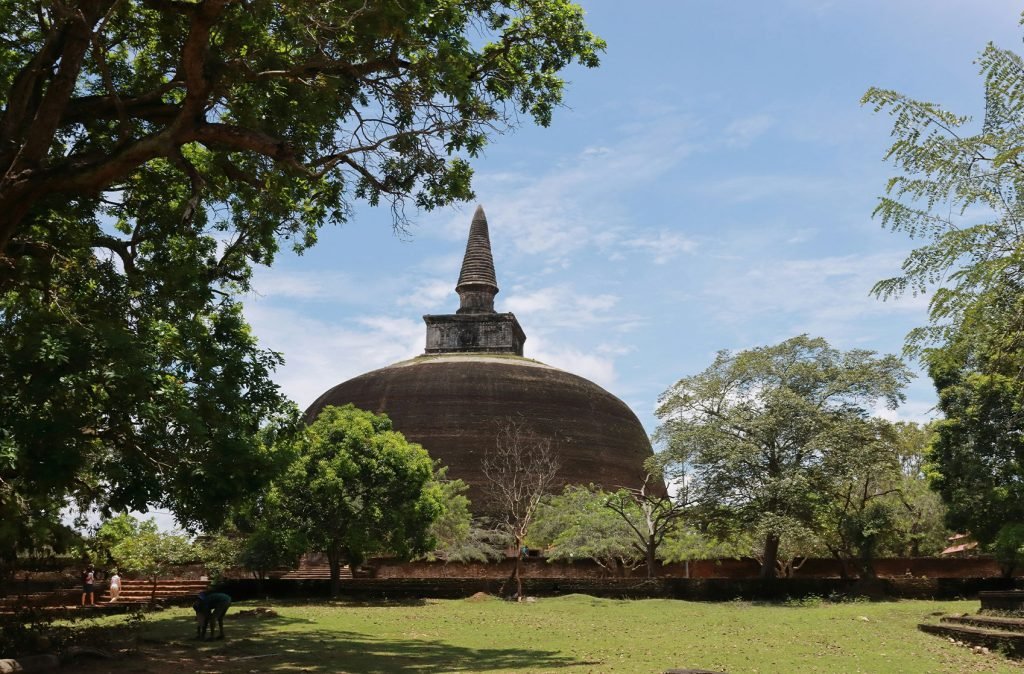 A large ancient stupa surrounded by greenery under a clear sky, showcasing historical religious landmarks