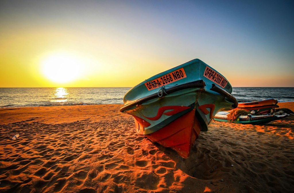 A colorful fishing boat beached on golden sand at sunset, reflecting the serene end to a coastal day